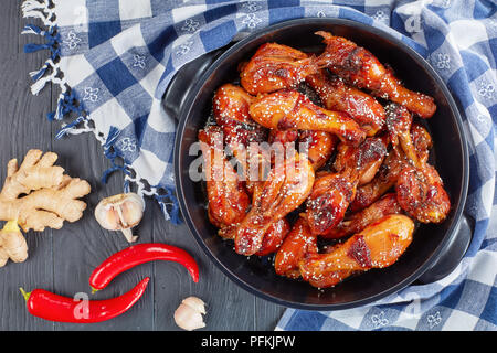 Lecker gegrilltes teriyaki Chicken Drumsticks bestreut mit Sesam in Schwarz brazier auf Holztisch mit Küchentuch, horizontale Ansicht von ab Stockfoto