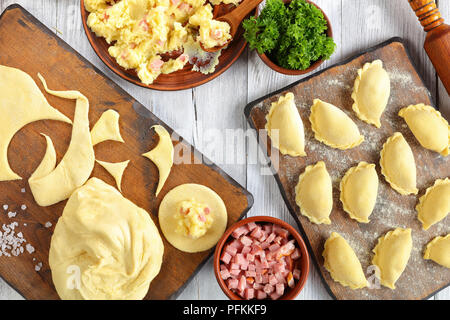 Die piroggen - traditionellen polnischen oder Ukrainischen Knödel. Kartoffelpüree, fein gehacktem Schinken oder Speck in Schalen, Teig auf Holz Schneidebrett und Ro Stockfoto