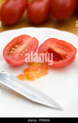 Rote Tomaten in Scheiben geschnitten auf Platte mit Samen und Messer Stockfoto