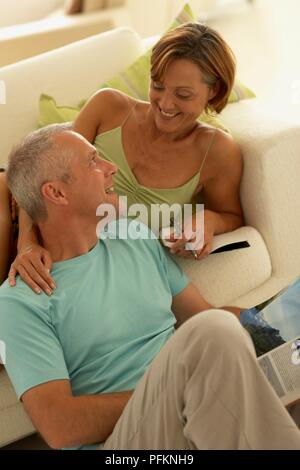 Liegende Frau auf Sofa holding Pen, Mann sitzt auf dem Boden neben ihr ein Magazin, bei jeder anderen suchen Lächeln Stockfoto