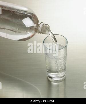 Gießen Wasser mit Kohlensäure aus Flasche in Glas Stockfoto