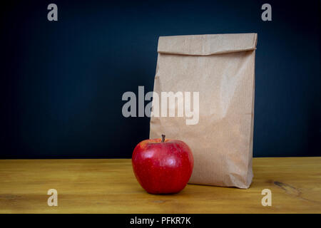 Schule Mittagessen. Braune Papiertüte und einen roten Apfel auf hölzernen Schreibtisch Stockfoto