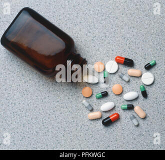 Bunte Auswahl an Pillen vor braunen Glasflasche zerstreut liegend auf seiner Seite, aus der Nähe. Stockfoto