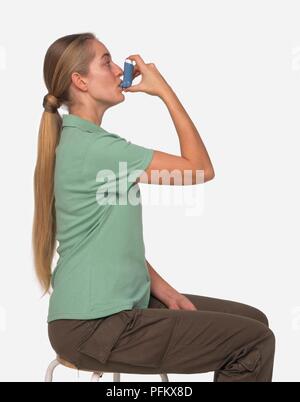 Frau mit langen Haaren sitzen auf Hocker und mit Inhalator, Seitenansicht Stockfoto