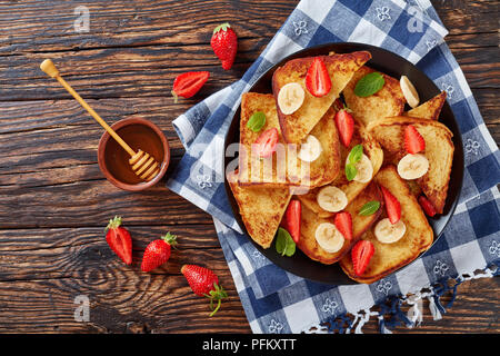 French Toast mit appetitlich goldbraune Kruste und flauschige Innenseite auf dem Teller serviert mit frischen Erdbeeren, Banane, Minze, Ahornsirup, fr Stockfoto