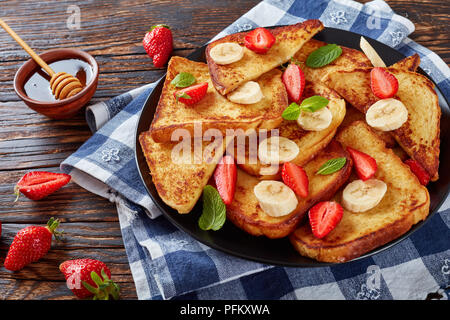 French Toast mit appetitlich goldbraune Kruste und flauschige Innenseite auf dem Teller serviert mit frischen Erdbeeren, Banane, Minze, Ahornsirup, fr Stockfoto