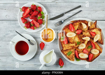 French Toast mit appetitlich goldbraune Kruste und flauschige Innenseite auf Platte mit frischen Erdbeeren, Banane, Minze, Ahornsirup, Kaffee und Stockfoto