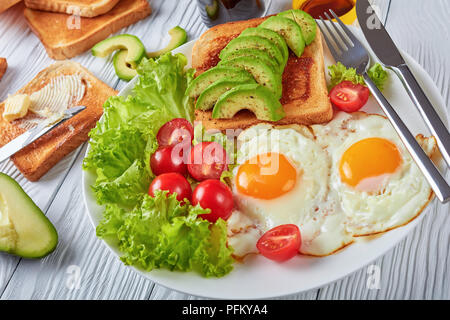 Gesunde aussie Frühstück - Spiegeleier, frische Salate, Toasts mit Hefe ausbreiten und in Scheiben geschnittenen Avocado auf einem weißen Teller auf einen hölzernen Tisch serviert, die Aussicht von ein Stockfoto