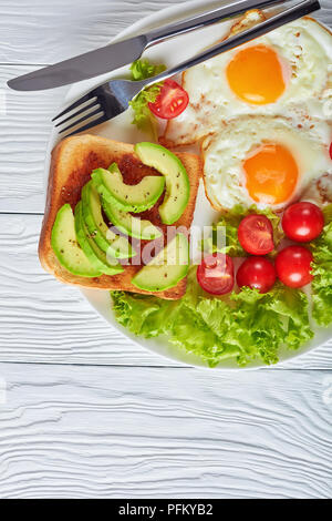 Gesunde australischen Frühstück - Spiegeleier, frische Salate, Toasts mit Hefe ausbreiten und in Scheiben geschnittenen Avocado auf einer weißen Platte auf einem Holztisch, vertikale Ansicht Stockfoto