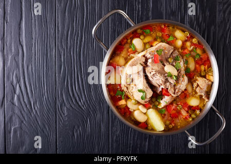 Köstliche reichen Schweinefleisch und Gemüse Suppe mit weißen Bohnen, grüne Erbsen und Arten in eine Kasserolle auf schwarzem Holz- Tabelle, Ansicht von oben Stockfoto