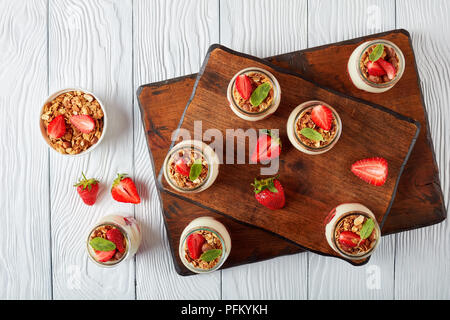 Köstliches hausgemachtes Müsli mit frischem Joghurt und reife Erdbeeren in Gläsern auf Schneidbretter, horizontale Ansicht von oben, flach Stockfoto