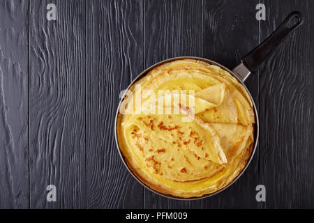 Frisch gebratene französische Crêpes in einer Pfanne auf schwarzem Holz- Tabelle, Ansicht von oben Stockfoto