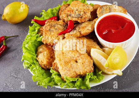 Der gebratene Stücke von Seehecht auf einer weißen Platte auf einer konkreten Tabelle mit Zitronenscheiben, Tomatensauce und Paprika, schließen, Ansicht von oben Stockfoto