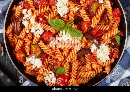 Vegetarische italienische Pasta Fusilli alla Norma mit Auberginen, Tomaten, Basilikum, ricotta Käse in einer Pfanne mit Zutaten im Hintergrund, Blick von Stockfoto