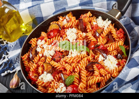 Italienische Pasta Fusilli alla Norma mit Auberginen, Tomaten, Basilikum, ricotta Käse in einer Pfanne mit Zutaten im Hintergrund, Ansicht von oben, Clos Stockfoto