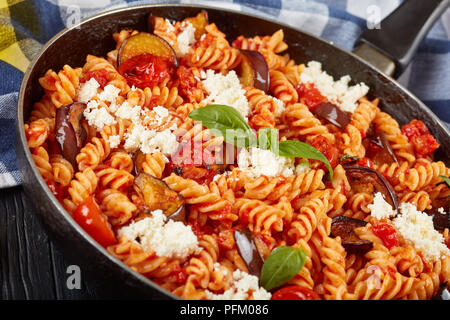 Vegetarische italienische Pasta Fusilli alla Norma mit Auberginen, Tomaten, Basilikum, ricotta Käse in einer Pfanne auf einem Holztisch, Ansicht von oben, close-up Stockfoto