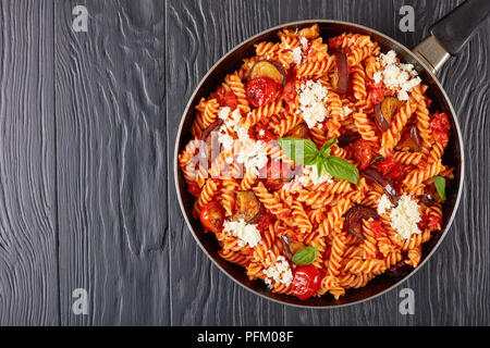 Italienische Pasta Fusilli alla Norma mit Auberginen, Tomaten, Basilikum, ricotta Käse in einer Pfanne auf einem schwarzen Holztisch, horizontale Ansicht von oben, Clos Stockfoto