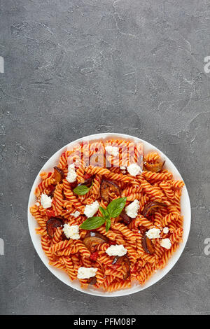 Italienische Pasta Fusilli alla Norma mit Auberginen, Tomaten, Basilikum, Ricotta in eine weiße Platte auf einer konkreten Tabelle, Ansicht von oben, flach Stockfoto