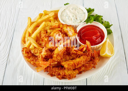 Close-up von leckeren knusprigen Cornflakes paniert und frittierte Garnelen auf einem Schild an einem Holztisch mit Pommes, Ketchup und coctail Soße in Stockfoto