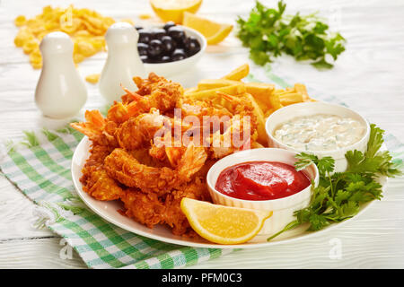 Crunchy Cornflakes paniert und frittierte Garnelen mit Pommes, Ketchup und Cocktail Sauce auf einer Platte auf einem Holztisch mit Zitronenscheiben und bl Stockfoto