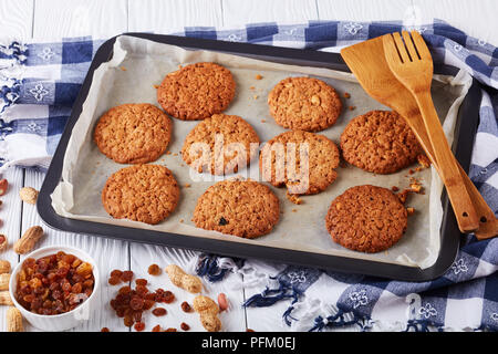 Frisch gebackene Oatmeal Cookies mit Rosinen und Erdnüsse auf ein Backblech mit Holzspatel und Küche Handtuch, horizontale Ansicht von oben, close-up Stockfoto