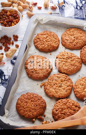Frisch gebackene Oatmeal Cookies mit Orangenschale, Rosinen und Erdnüsse auf ein Backblech mit Holzspatel und Küche Handtuch, Ansicht von oben, in der Nähe - u Stockfoto