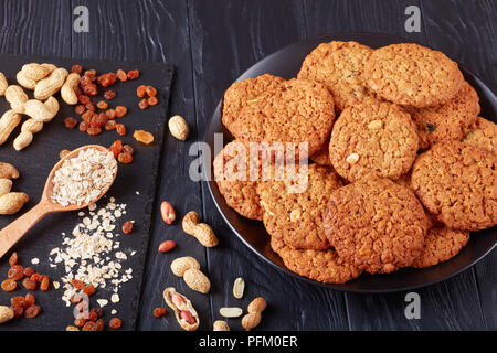 Brauner Zucker Haferflocken Rosinen und peanut Cookies auf eine schwarze Platte mit Zutaten auf einer Schiefertafel Fach, Ansicht von oben, close-up Stockfoto
