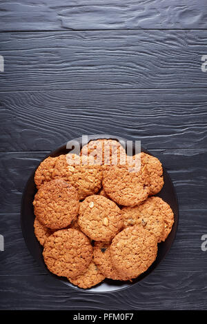 Leckere Haferflocken Rosinen und peanut Cookies auf einer schwarzen Platte auf einem Holztisch, Ansicht von oben, flach Stockfoto