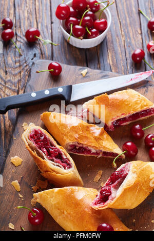 In der Nähe von frisch gebackenen cherry Strudel auf einem hölzernen Schneidebrett mit frischen Kirschen im Hintergrund, vertikale Ansicht von oben Stockfoto