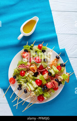 Gegrilltes Hühnerfleisch Shish Kebab Spieße mit Zucchini Bänder, Tomaten, Mozzarella Kugeln, Salami Scheiben, schwarze Oliven auf eine weiße Platte, vertikale v Stockfoto