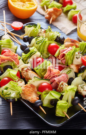 Zucchini ribbon Salat auf Spieße mit Hähnchenfleisch, Tomaten, Mozzarella Kugeln, Salami, Oliven auf einer schwarzen Platte auf einem Holztisch mit frischen Orange Ju Stockfoto