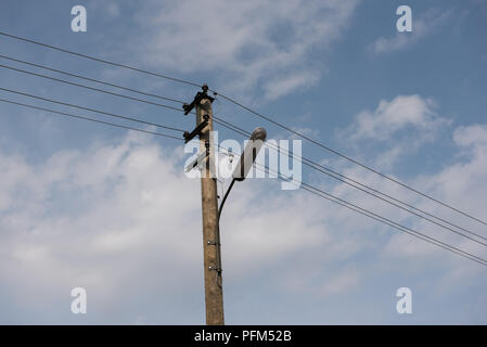 Holz- Street Lamp Post mit elektrischen Leitungen gegen den blauen Himmel mit weißen Wolken Stockfoto