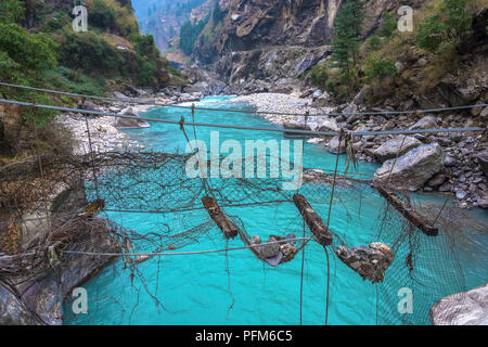 Alten zerstörten Hängebrücke über den stürmischen mountain river im Himalaya, Nepal. Stockfoto