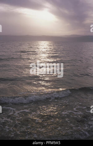 Sonnenaufgang über dem Meer bei Reifen, Libanon, Sonne auf dem Wasser und Wellen, Berge im Hintergrund mit Wolken über Rolling widerspiegelt. Stockfoto