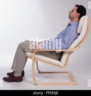 Mann sitzt im Stuhl mit seinen Augen legte sich geschlossen, Seitenansicht Stockfoto