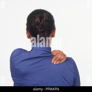 Rückansicht einer Frau, die ihre Schulter mit der Hand zu massieren, Stockfoto