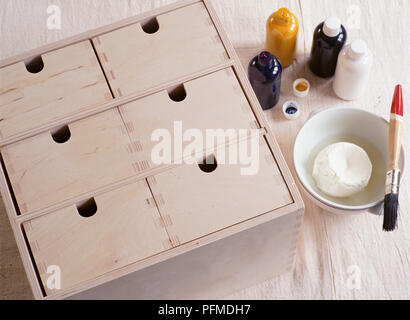 Kleine Holz- Schubladen, Klumpen aus Milch Quark in Schüssel weiß mit Pinsel ruht auf Seite, kleinen gelben, blauen und gelben Töpfe von Farbe mit Deckel entfernt, oben betrachten. Stockfoto