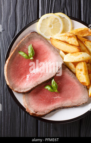 Saftig gegrilltes Rindersteak mit Bratkartoffeln und Zitrone close-up auf einem Teller auf dem Tisch. Senkrechte Draufsicht von oben Stockfoto