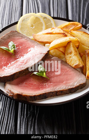 Medium gebratenem Rindfleisch Steak mit Kartoffeln close-up auf einem Schild auf einem Schwarzen Tisch. Vertikale Stockfoto