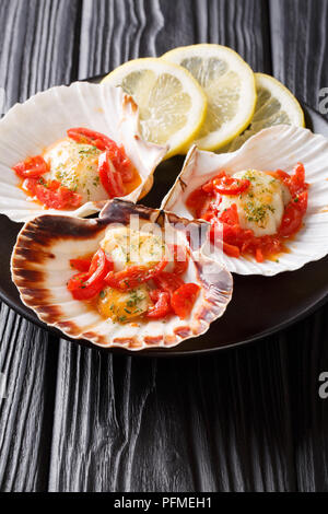 Gesunde Nahrungsmittel Meeresfrüchte: jakobsmuscheln in einer Shell mit Sauce, Tomaten und grünen Close-up auf einem Teller auf dem Tisch. Vertikale Stockfoto