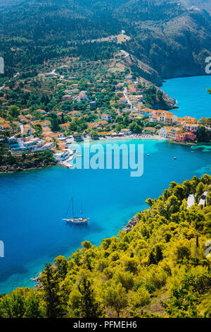 Assos Dorf im Morgenlicht, Kefalonia. Griechenland. Weiße einsame Yacht in wunderschönen türkisfarbenen Lagune Wasser von Pinien und Zypressen entlang der Küste umgeben Stockfoto