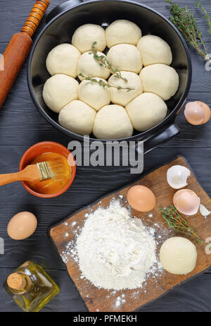 Ungebackene weich und flauschig Abendessen Rollen in Auflaufform mit Teig, Mehl und Ei auf einem Schneidebrett und Rolling Pin auf Holz- Küche Arbeitsplatte, vertikal Stockfoto