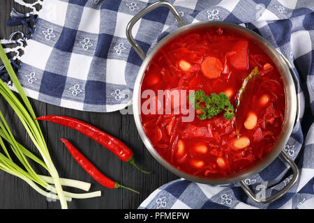 Köstliche rote Beete rote Suppe mit weißen Bohnen oder Borschtsch in Edelstahl Kasserolle Pfanne mit Handtuch, Chili und Frühlingszwiebeln auf Tisch, authentische recip Stockfoto