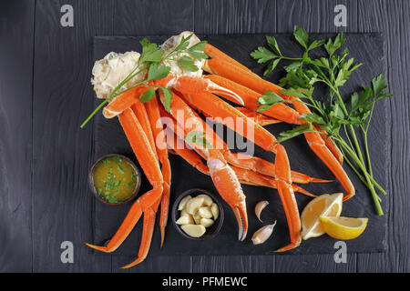 Gekochte Krabben Beine mit zerlassener Butter Sauce, Knoblauch und Petersilie auf schwarzen Stein Fach, auf Holz- Tabelle, Ansicht von oben Stockfoto