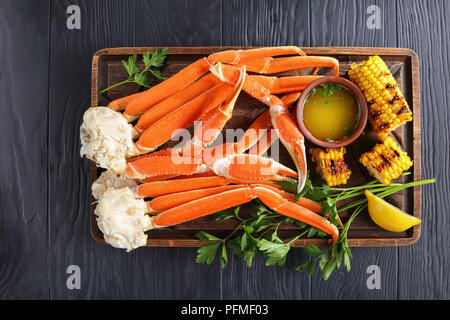 Nahaufnahme der gekochten Krebsscheren mit zerlassener Butter, Knoblauch, Nelken, Zitronenscheiben und frische Petersilie auf alten hölzernen Schneidebrett mit gegrilltem Mais, Maiskolben, Stockfoto