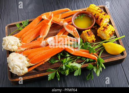 Gedämpfte Krabben mit zerlassener Butter, Knoblauch, Nelken, Zitronenscheiben, gegrilltem Mais, Maiskolben und frische Petersilie auf alten hölzernen Schneidebrett, auf Schwarz Holz- Stockfoto