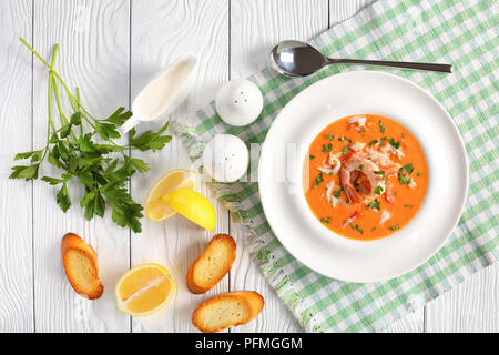 Köstlichen heißen bisque von Geschredderten alaskan Krebsfleisch, Garnelen und Gemüse in einem weißen breiten Felge Soup Bowl auf Holztisch mit Löffel, geröstetes Brot ein Stockfoto