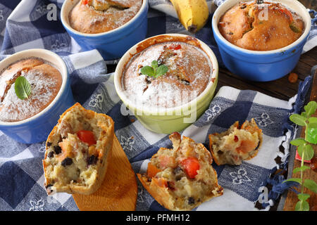 Leckere frisch gebackene selbstgemachte Banane Mutter raisin Muffins bestreut mit Puderzucker in Keramik förmchen und ein Muffin wurde in Stücke gebrochen an Stockfoto