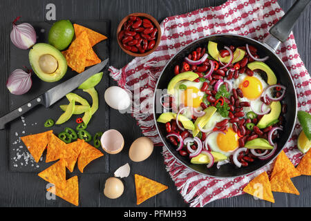 Leckeres mexikanisches Frühstück - Spiegeleier, rote Bohnen, Avocado, Scheiben, Zwiebelringe, Hot Chili und jalapeno Pfeffer auf Skillet, Zutaten und Nachos o Stockfoto