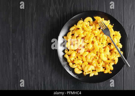 Klassische gebackene Hausgemachte Makkaroni und Käse auf schwarzem Teller mit Gabel auf dunklen Holz- Tabelle, Ansicht von oben Stockfoto